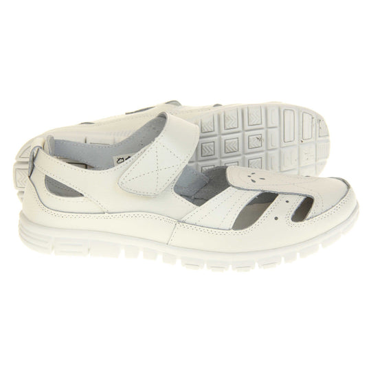 Womens white wide fit sandals. Mary Jane style shoes. White leather uppers with white stitching detail. White touch fasten strap over the foot. Cut outs in the middle, edges and heel of the shoes. White sole with grip to the bottom. Both feet from a side profile with left foot on its side behind the right to show the sole.